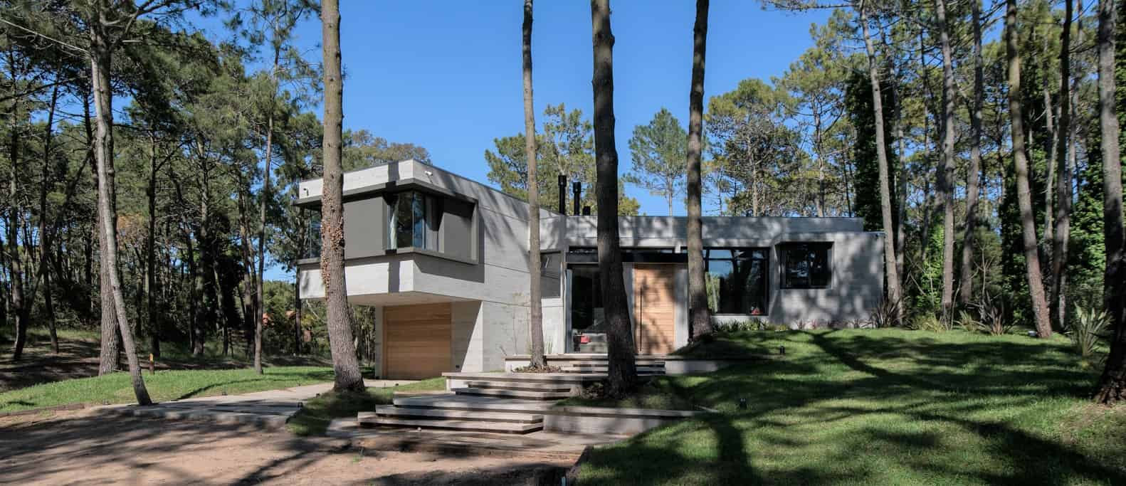 Modern minimalist house design with large windows, clean lines, and a concrete exterior set in a lush forest environment. Perfect example of contemporary architecture blending with nature.