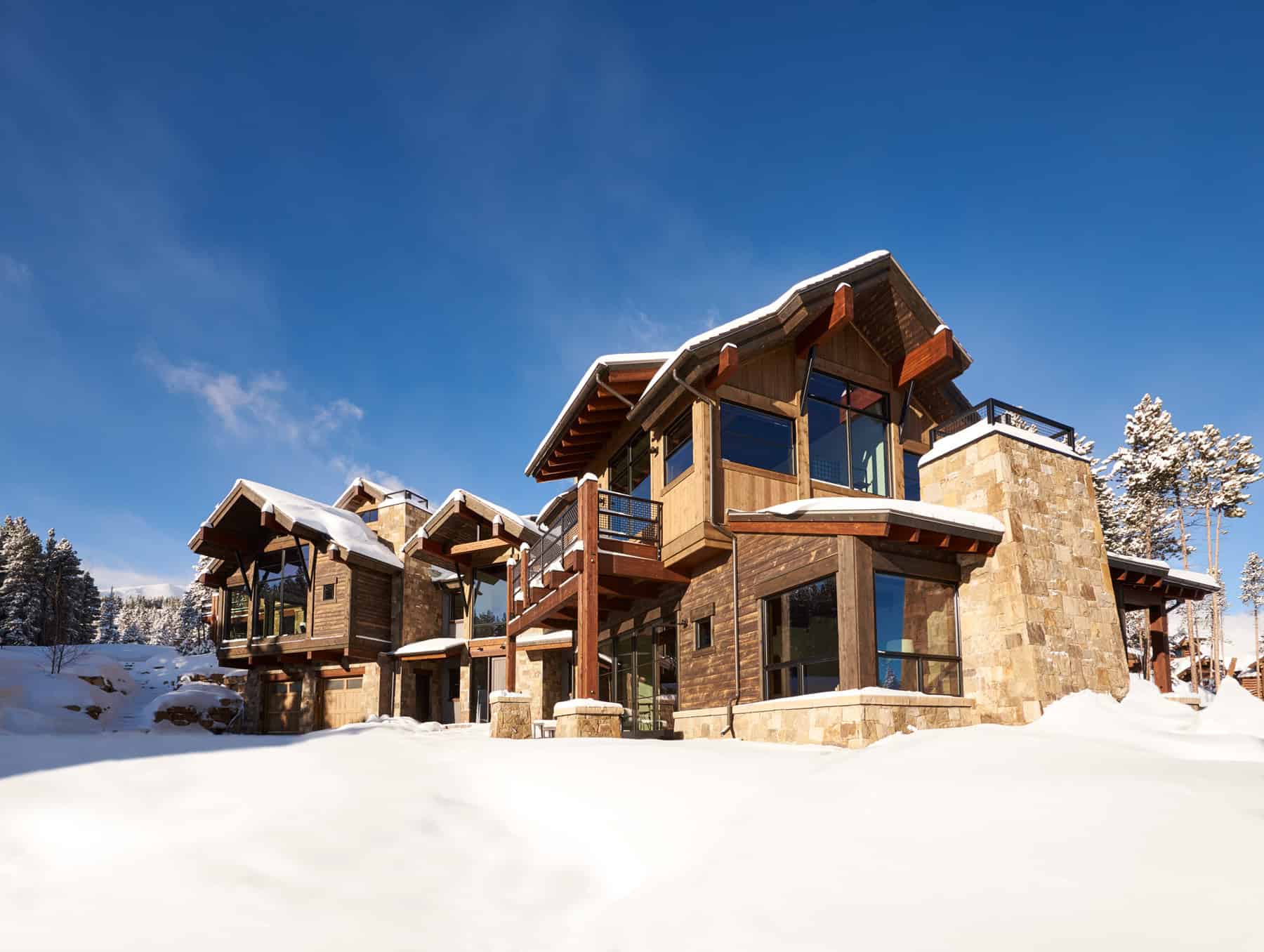 Contemporary mountain lodge with large glass windows, wooden accents, and snow-covered roof, blending modern architecture with natural surroundings.