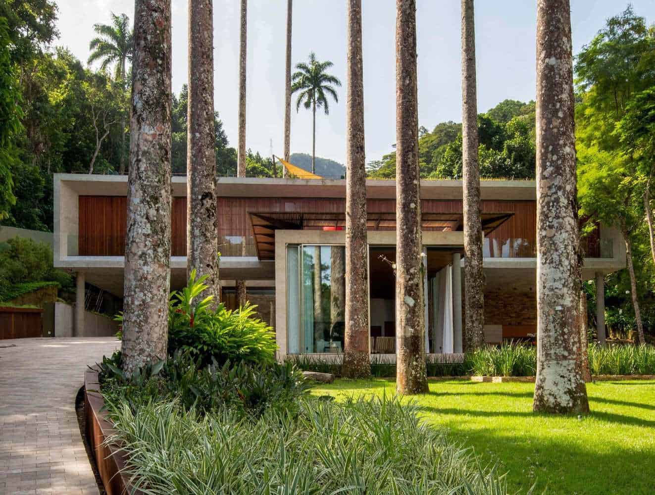 Modern luxury house surrounded by tall trees and lush greenery, showcasing contemporary architectural design with wood and concrete elements, set in a tropical forest environment.