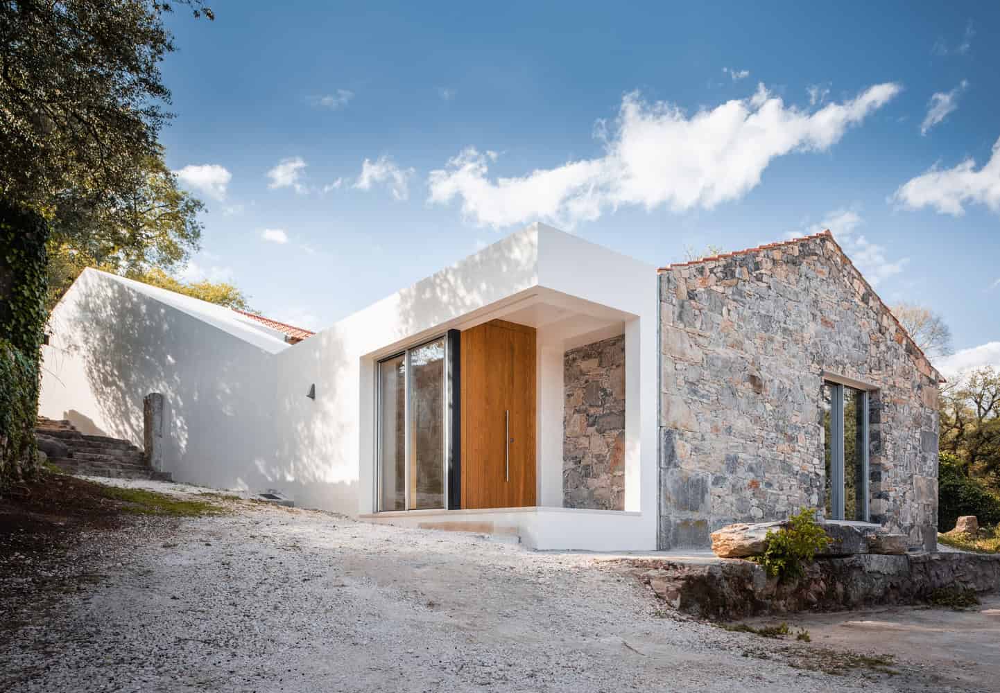 Contemporary modern house with minimalist design, white walls, natural stone accents, and large glass doors, blending sleek architecture with rustic stone elements, set in a scenic outdoor environment.