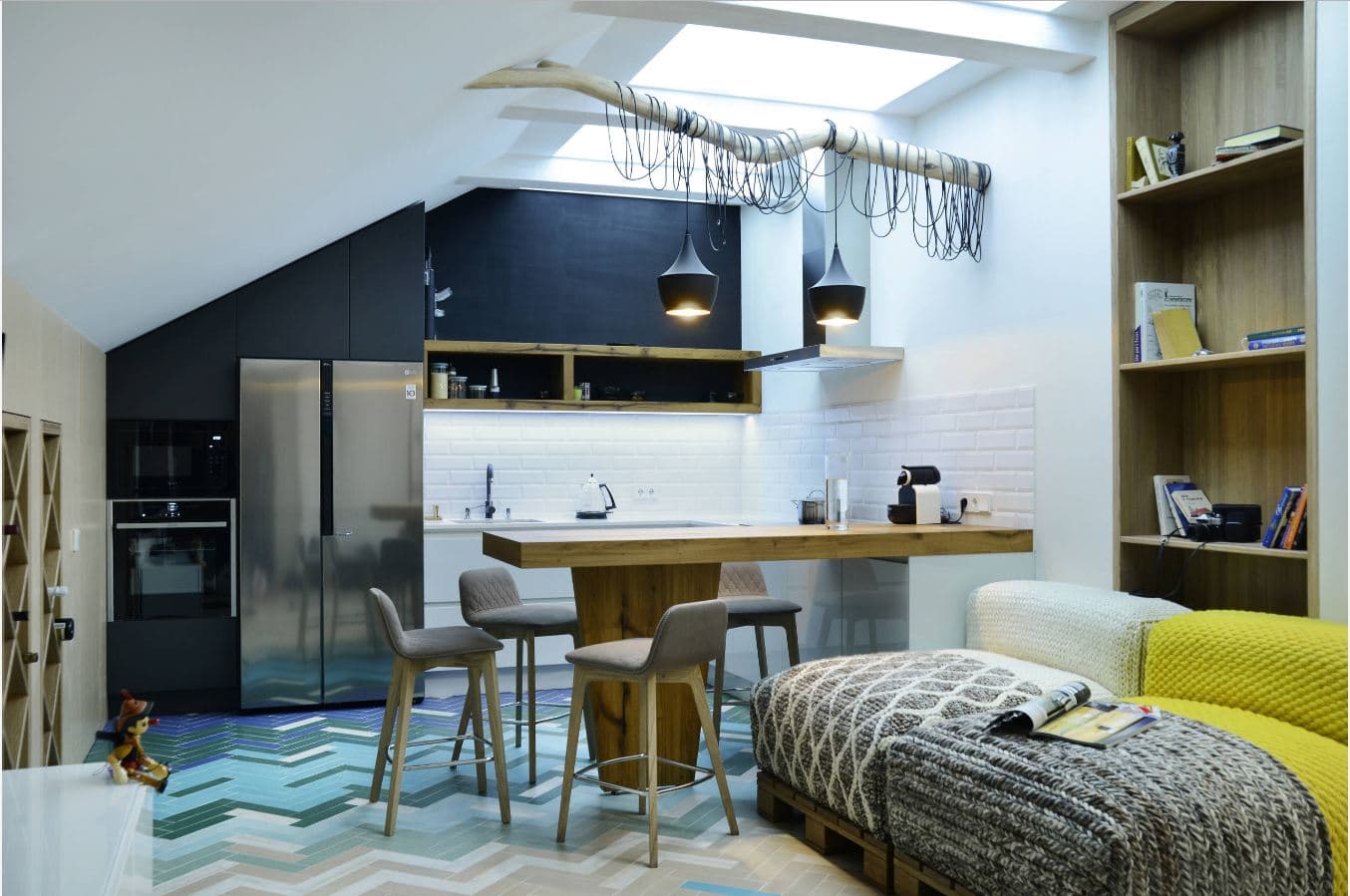 Modern loft-style small kitchen with black cabinetry, stainless steel appliances, and cozy dining area featuring wooden accents and colorful geometric patterned flooring.