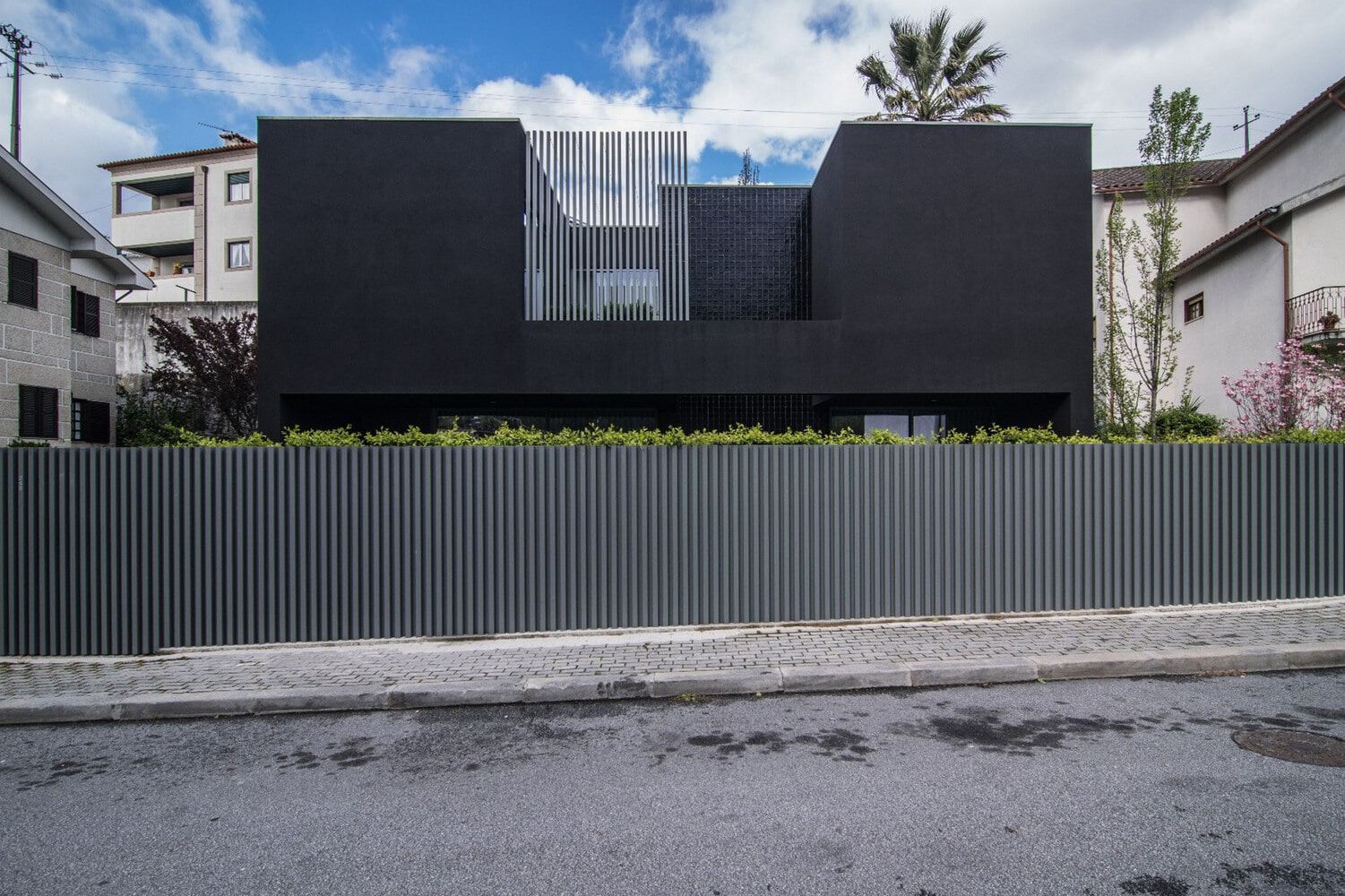 Sleek modern black house with contemporary architectural design, featuring clean lines and a minimalist facade, surrounded by greenery and urban environment.