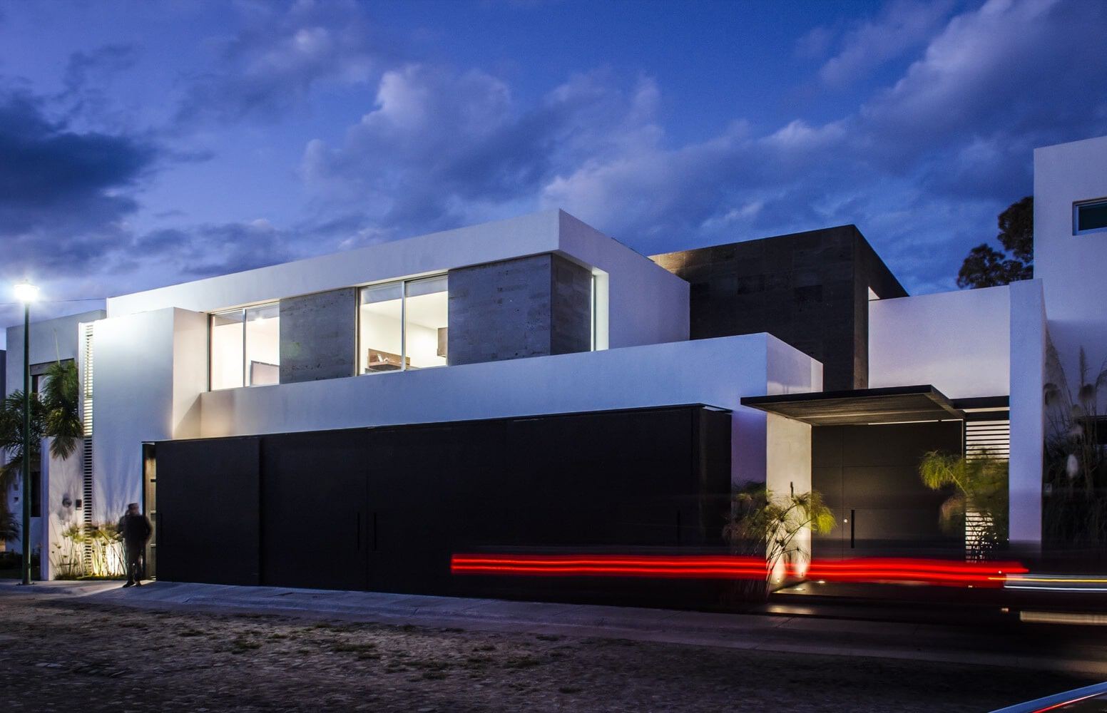 Modern minimalist house with sleek black and white exterior walls, large glass windows, and contemporary architectural design under a partly cloudy evening sky.