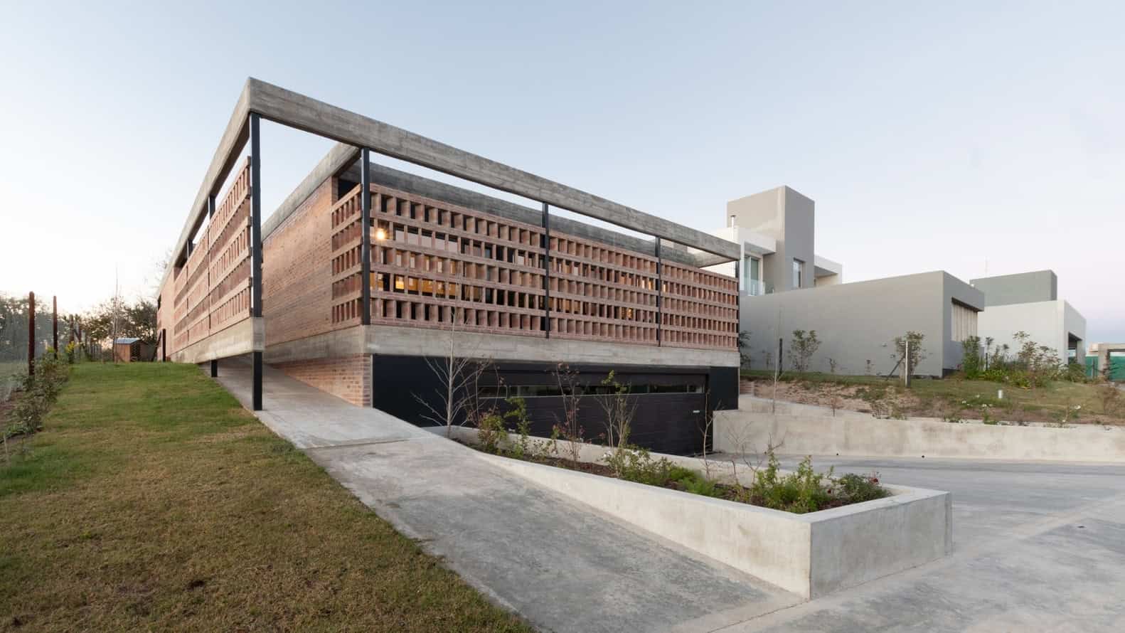 Modern contemporary building with unique brick lattice facade and minimalist architectural design, set on a gently sloping landscaped lot.