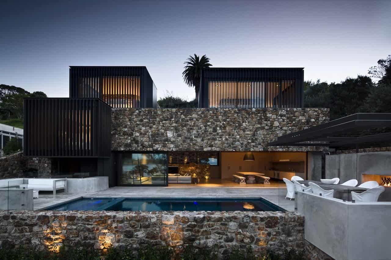 Modern luxury house with a stone and metal exterior, outdoor swimming pool, and stylish outdoor seating, showcasing contemporary architecture and innovative design.