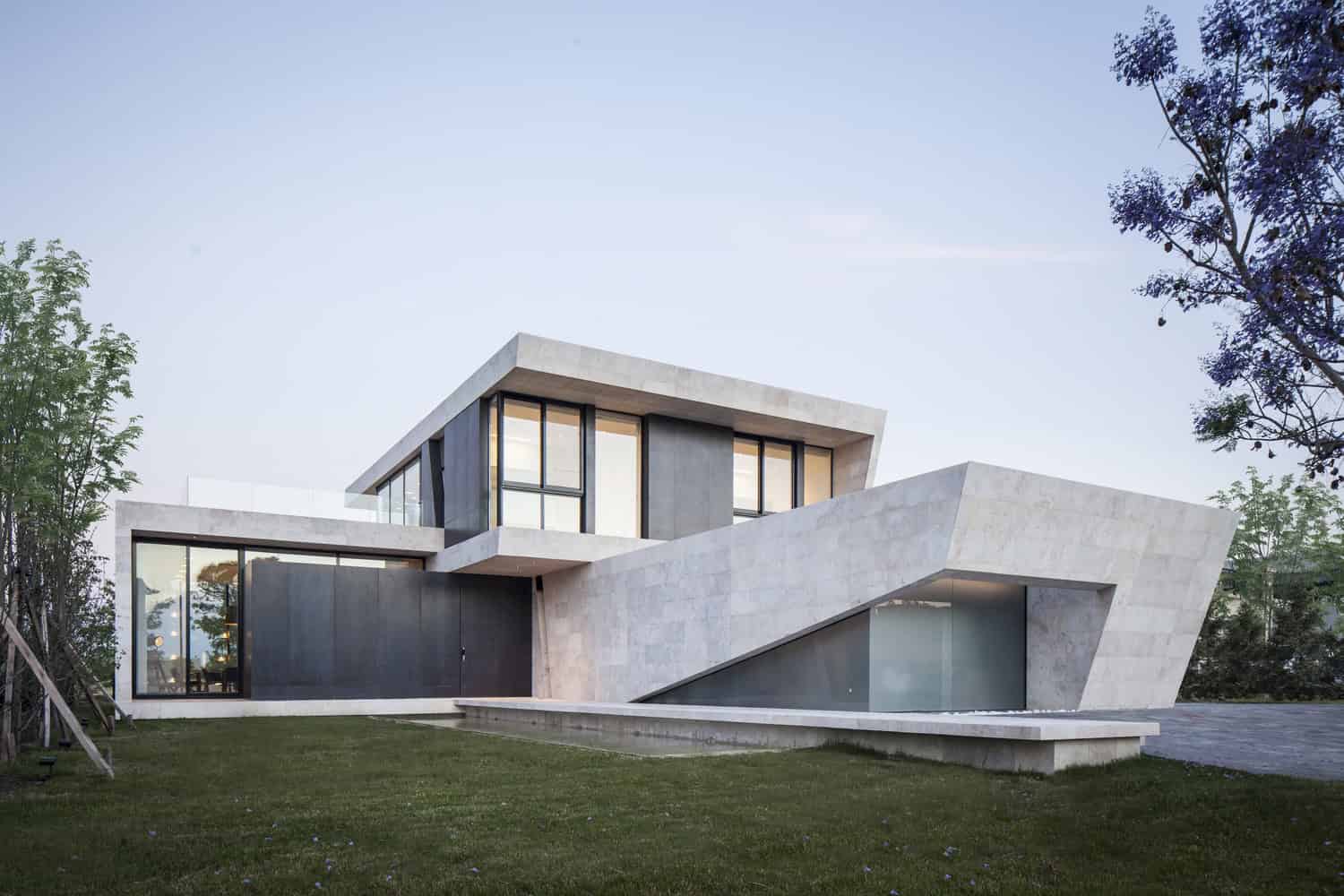 Sleek modern concrete house with large windows and geometric design, surrounded by greenery, showcasing contemporary architecture and innovative home design.