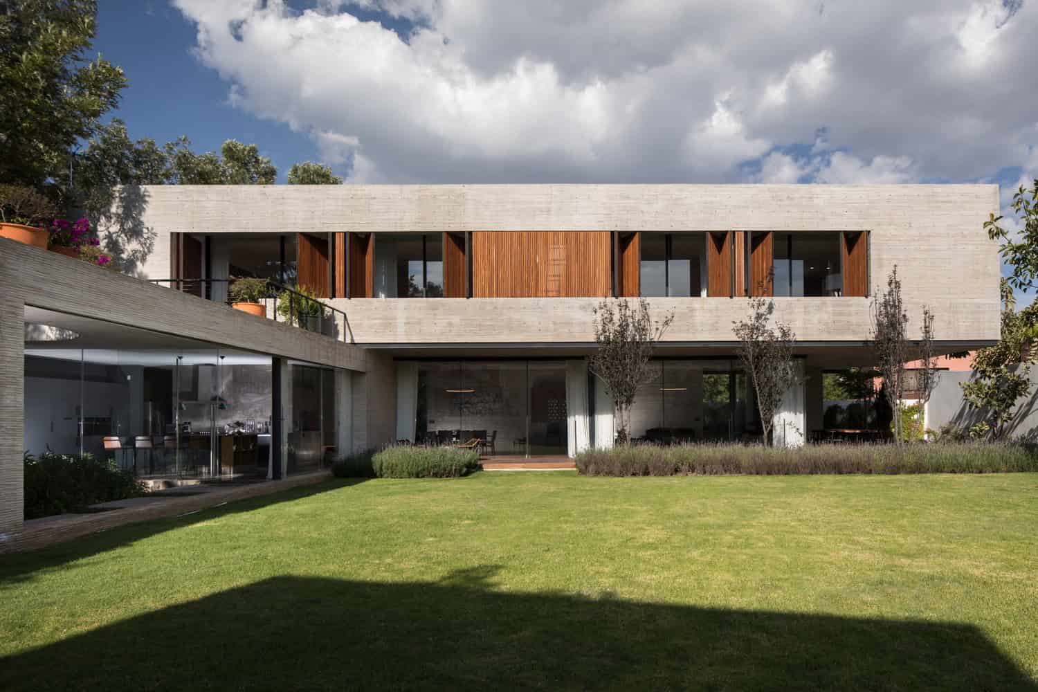 Modern minimalist house with concrete and wood facade, large glass windows, and lush green lawn, showcasing contemporary architecture and innovative design elements.