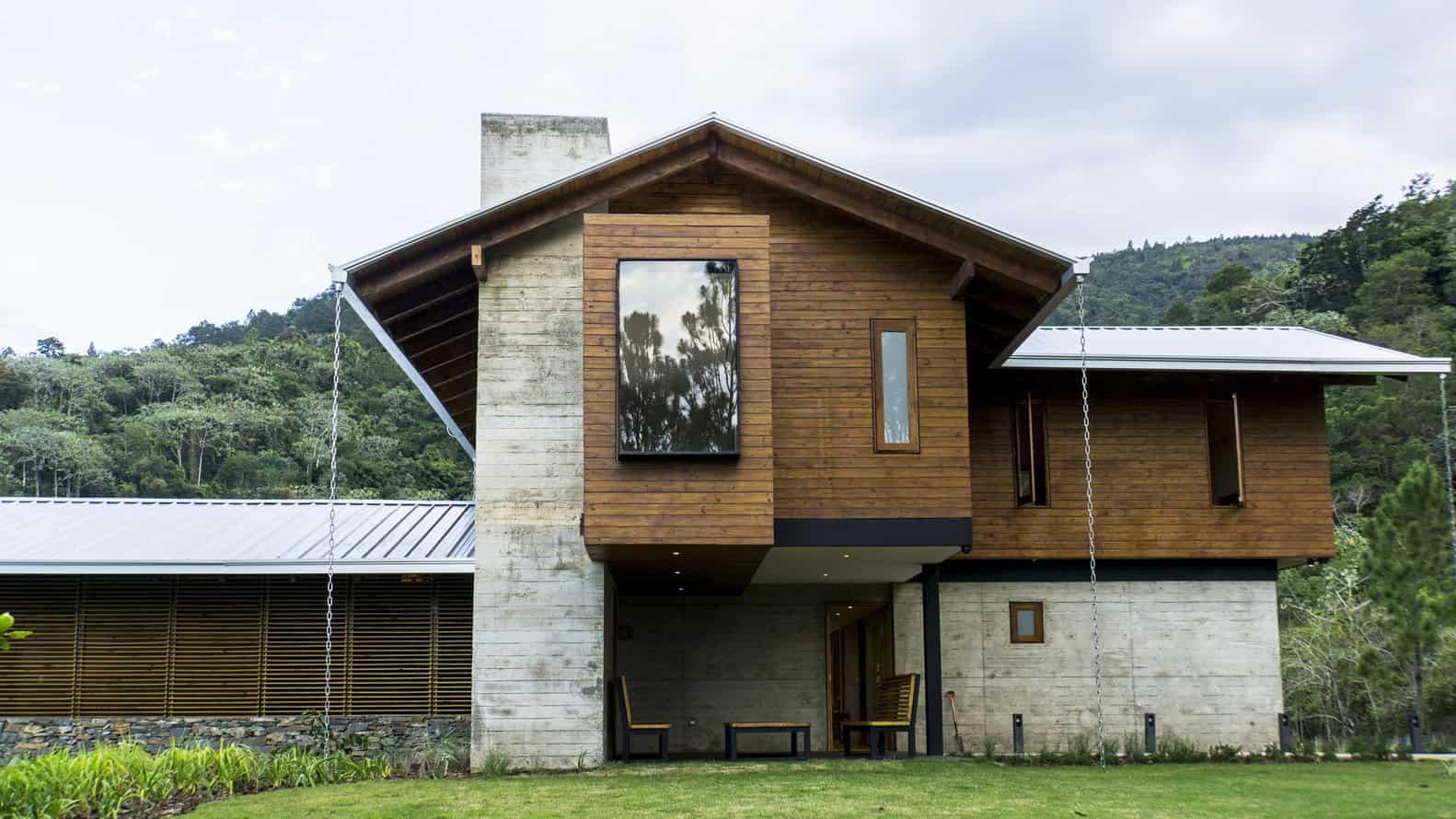 Contemporary mountain home featuring modern architecture with wooden facade and large windows blending with lush green landscape.