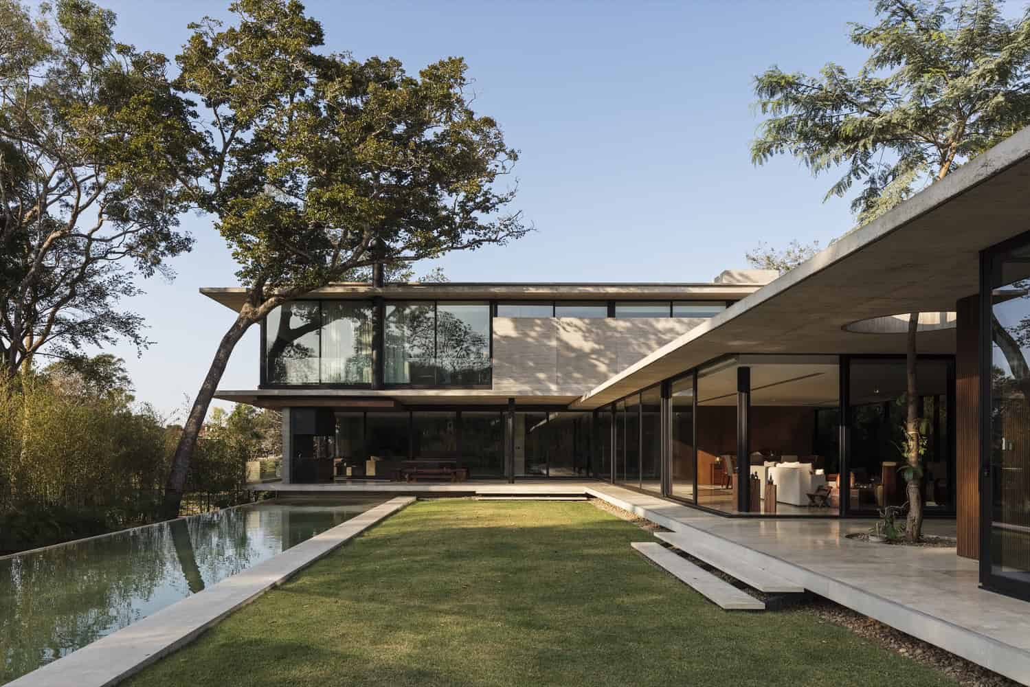 Modern luxury home with expansive glass windows, minimalist design, and seamless indoor-outdoor living spaces surrounded by lush greenery.