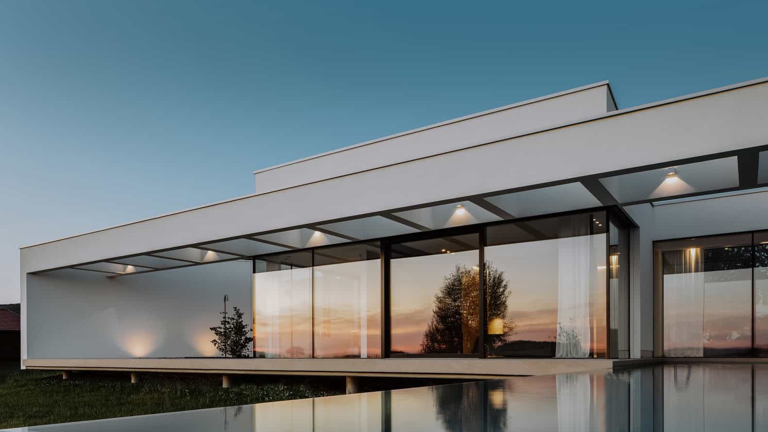 Contemporary modern architecture house with large glass windows and minimalist design at sunset.