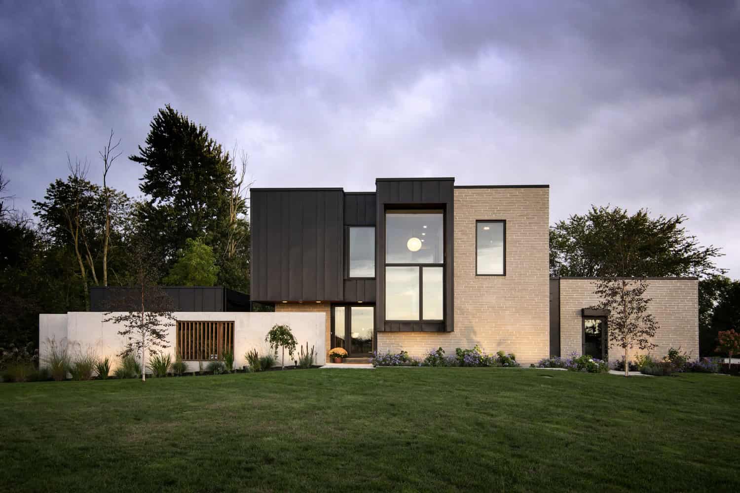 Contemporary modern house with sleek black metal and beige brick facade, large windows, and landscaped lawn, showcasing innovative architectural design and stylish exterior.