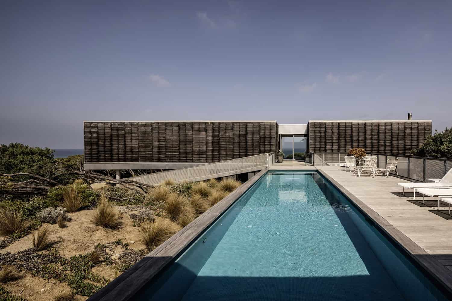 Contemporary modern house with a sleek outdoor swimming pool and minimalist architecture, featuring natural wood finishes and expansive outdoor lounge area on a scenic elevated landscape.