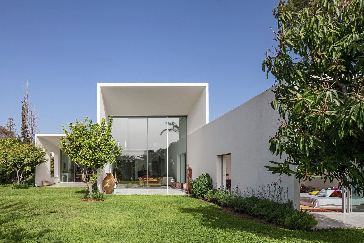 Modern minimalist white house with large glass windows, sleek architectural design, and lush garden landscape showcasing contemporary residential architecture.