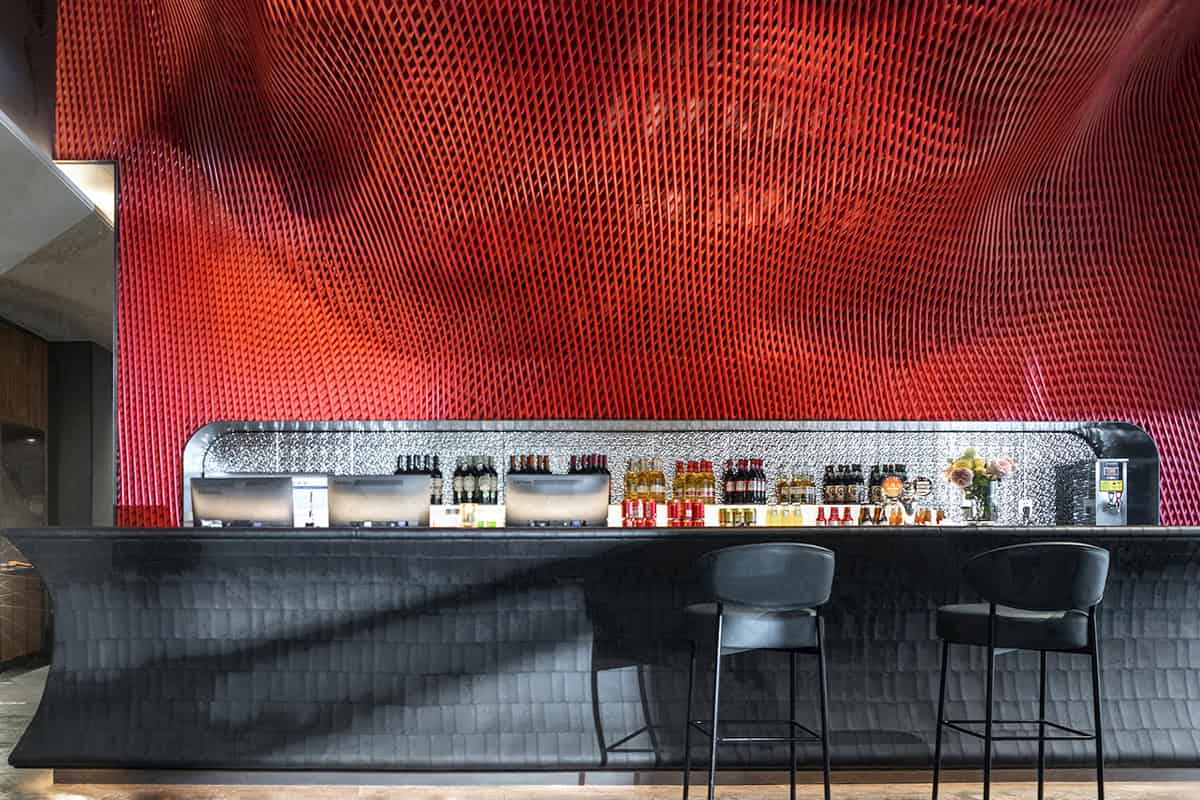 Vibrant red textured wall behind a modern bar with sleek black seating and a variety of bottles on display, showcasing contemporary restaurant interior design and architectural art styles.