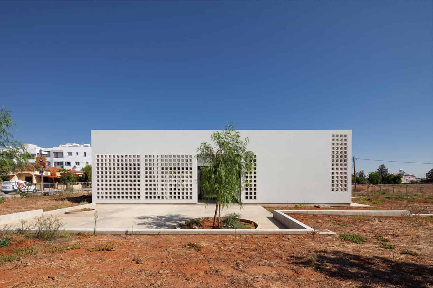 Modern minimalist white architectural building with geometric perforated concrete wall design, set against a clear blue sky, emphasizing contemporary architecture and innovative construction techniques.