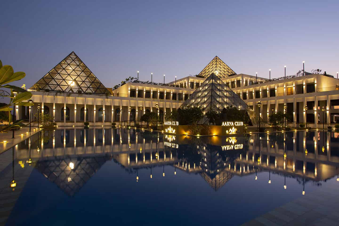 Modern luxury resort with illuminated glass pyramid structures and elegant architecture reflected in a serene pool at dusk. Perfect for upscale travel and vacation destinations.