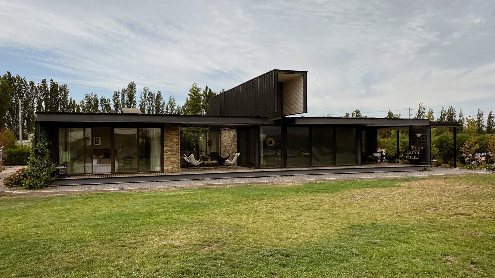 Modern black minimalist house with large glass sliding doors, outdoor patio, and green landscape, showcasing contemporary architecture and innovative design elements.