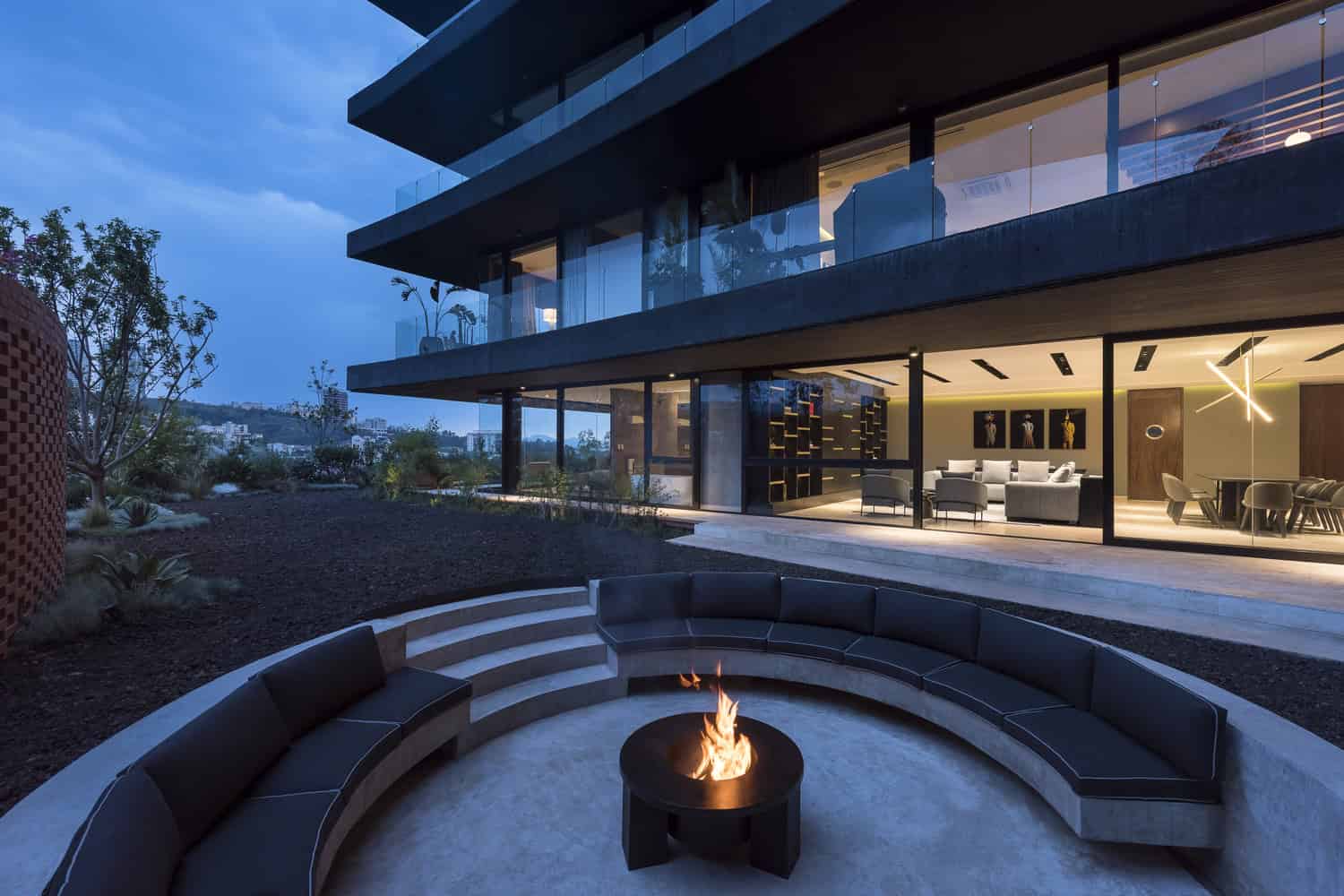 Sleek modern house with large glass windows, outdoor firepit, and contemporary outdoor seating area, showcasing luxury residential architecture and innovative design.