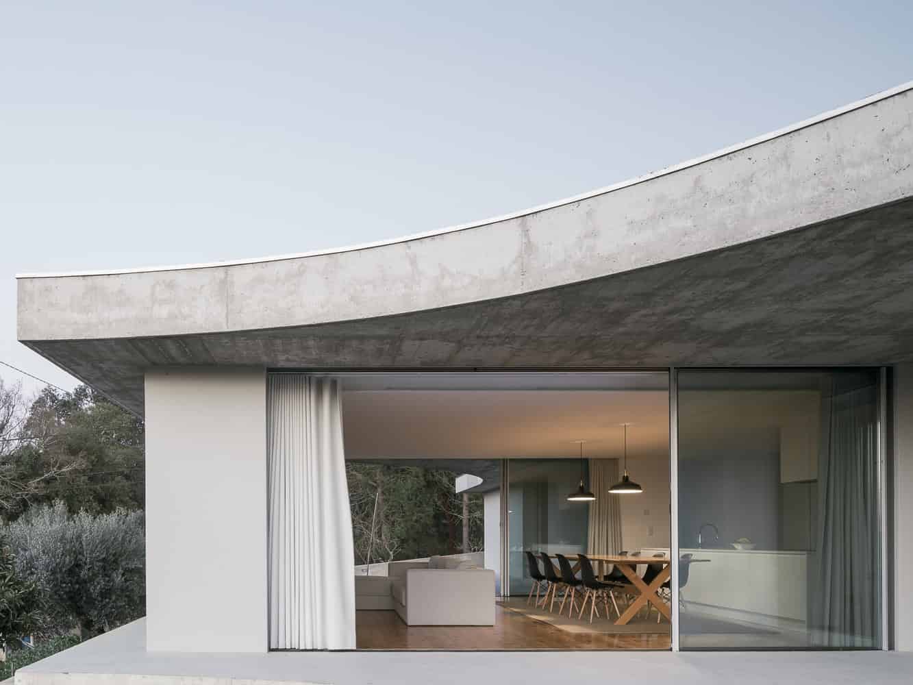 Contemporary modern house featuring large glass sliding doors, minimalist design, concrete accents, and an open-plan interior with dining area and living space, ideal for modern architecture and home design.