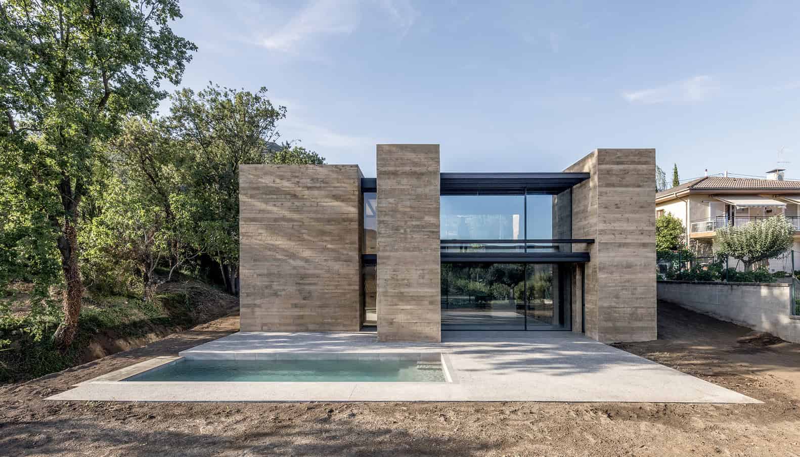 Contemporary modern house with minimalist design, featuring large glass windows, sleek lines, and natural stone facade amidst greenery for luxury architecture.