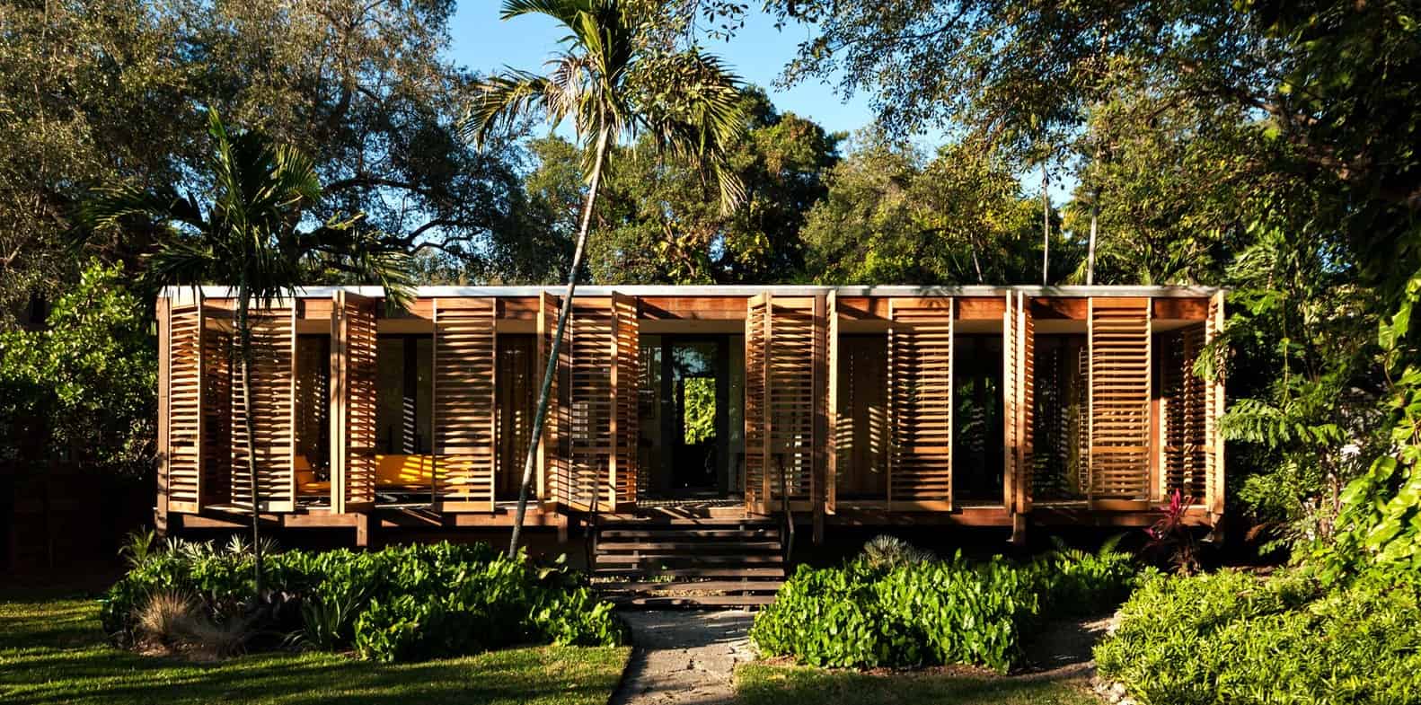 Contemporary wooden vacation cabin with slatted exterior design surrounded by lush tropical greenery in a serene natural setting.