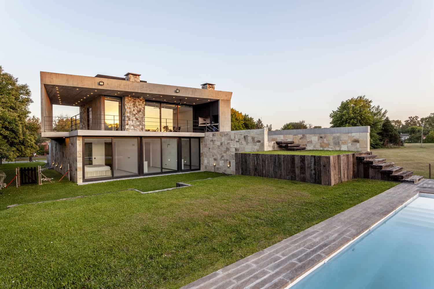 Contemporary modern house with large glass doors, stone accents, and a spacious backyard with a pool, showcasing innovative architecture and design.