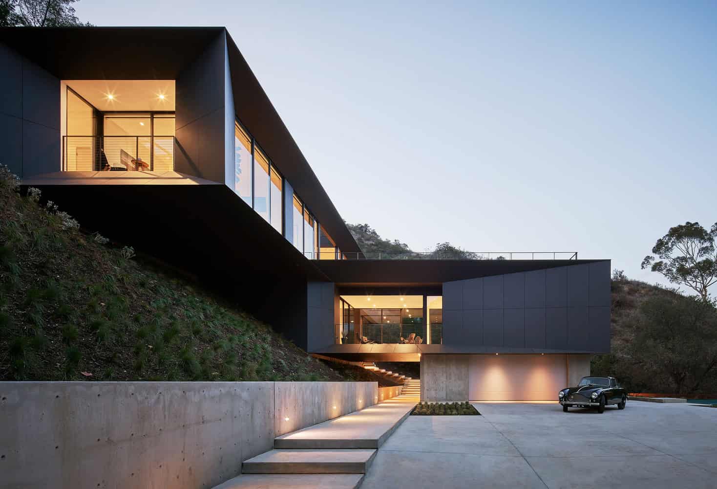 Contemporary modern house with sleek black exterior, large glass windows, and hillside setting showcasing innovative architecture and modern residential design.