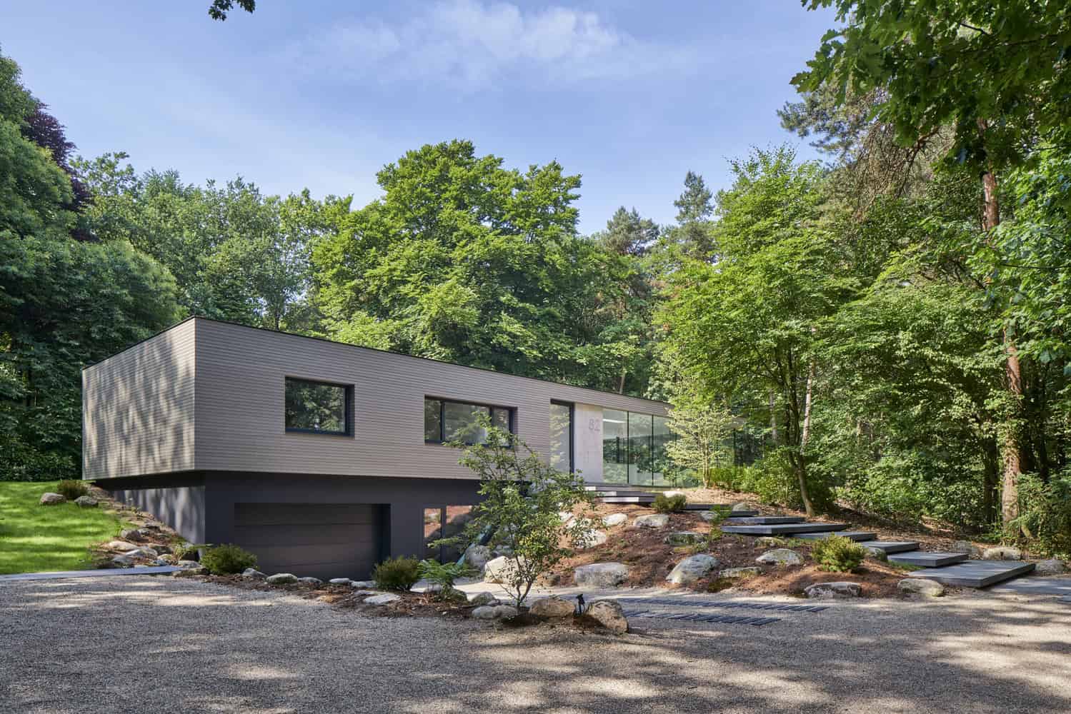 Contemporary modern house with sleek design, large glass windows, and minimalist exterior, nestled in lush green forest setting, showcasing innovative architecture and sustainable living.