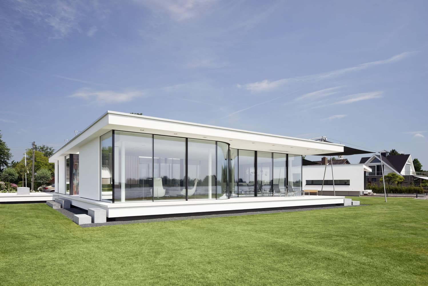 Contemporary modern glass house with sleek white exterior, expansive floor-to-ceiling windows, and minimalist design set in a lush green landscape. Ideal for luxury architecture and innovative home design.