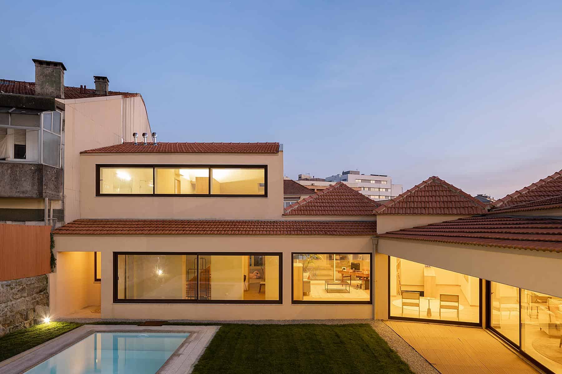 Contemporary modern house exterior with large glass windows, red tiled roof, backyard pool, and stylish interior lighting, showcasing innovative architecture and design.