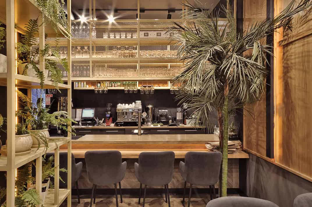 Modern restaurant interior with a cozy bar counter, stylish seating, lush indoor plants, and warm lighting, showcasing contemporary architecture and chic design elements.