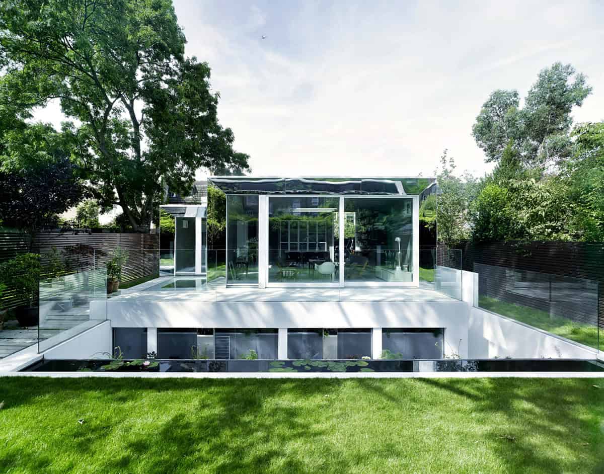Modern glass house with sleek architectural design, surrounded by lush greenery and landscaped garden, featuring contemporary aesthetics and outdoor living space.