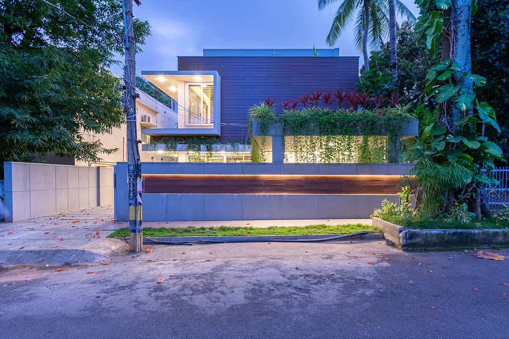 Modern contemporary house with sleek design, lush garden, and urban street setting, showcasing innovative architecture and stylish exterior lighting.