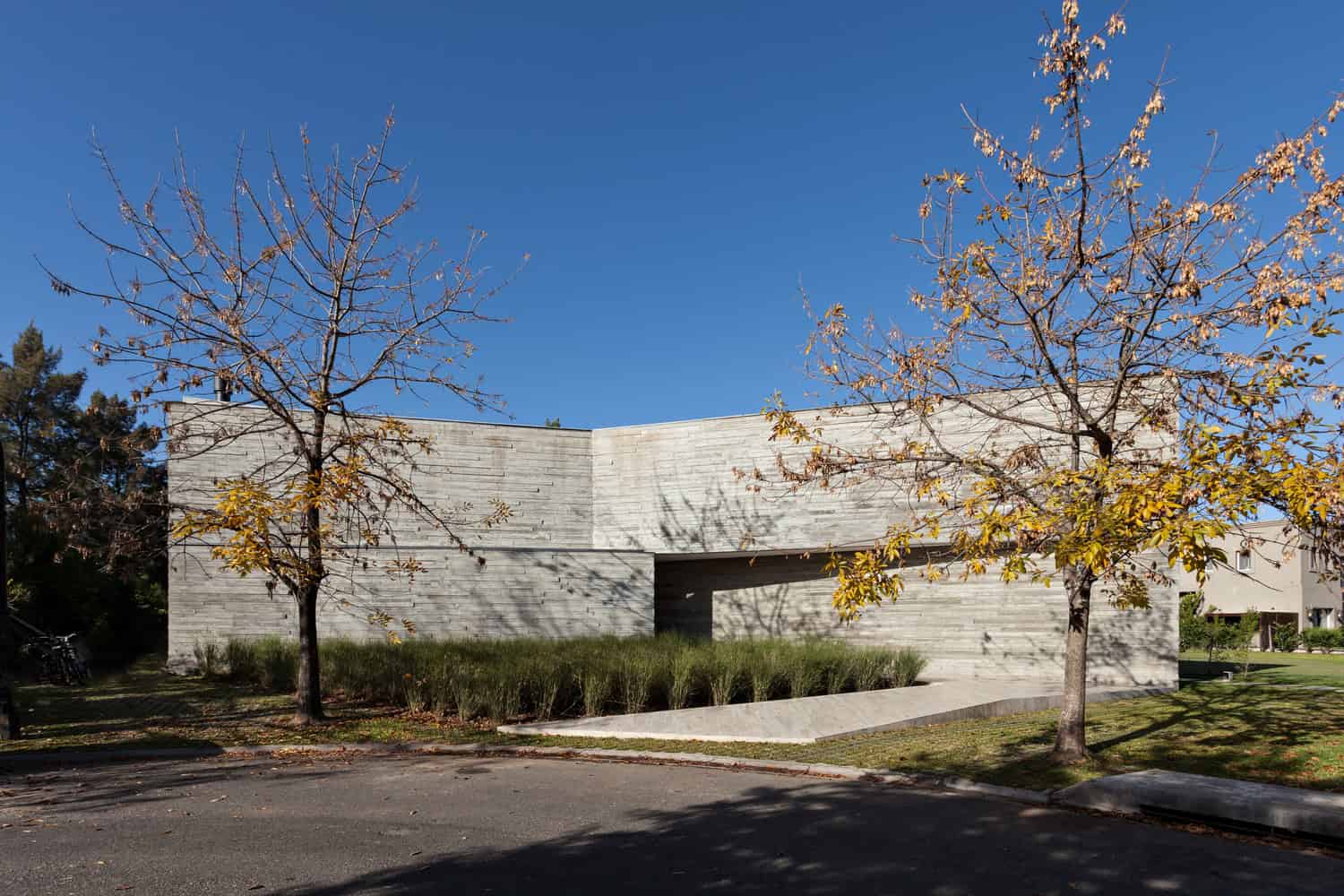 Contemporary concrete architecture with minimalist design, clean lines, and modern urban landscaping featuring autumn trees and clear blue sky.