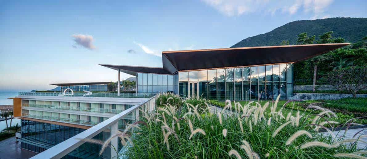 Contemporary modern architecture hotel with sleek glass facades and striking roof design nestled in lush green landscape and scenic mountain backdrop.