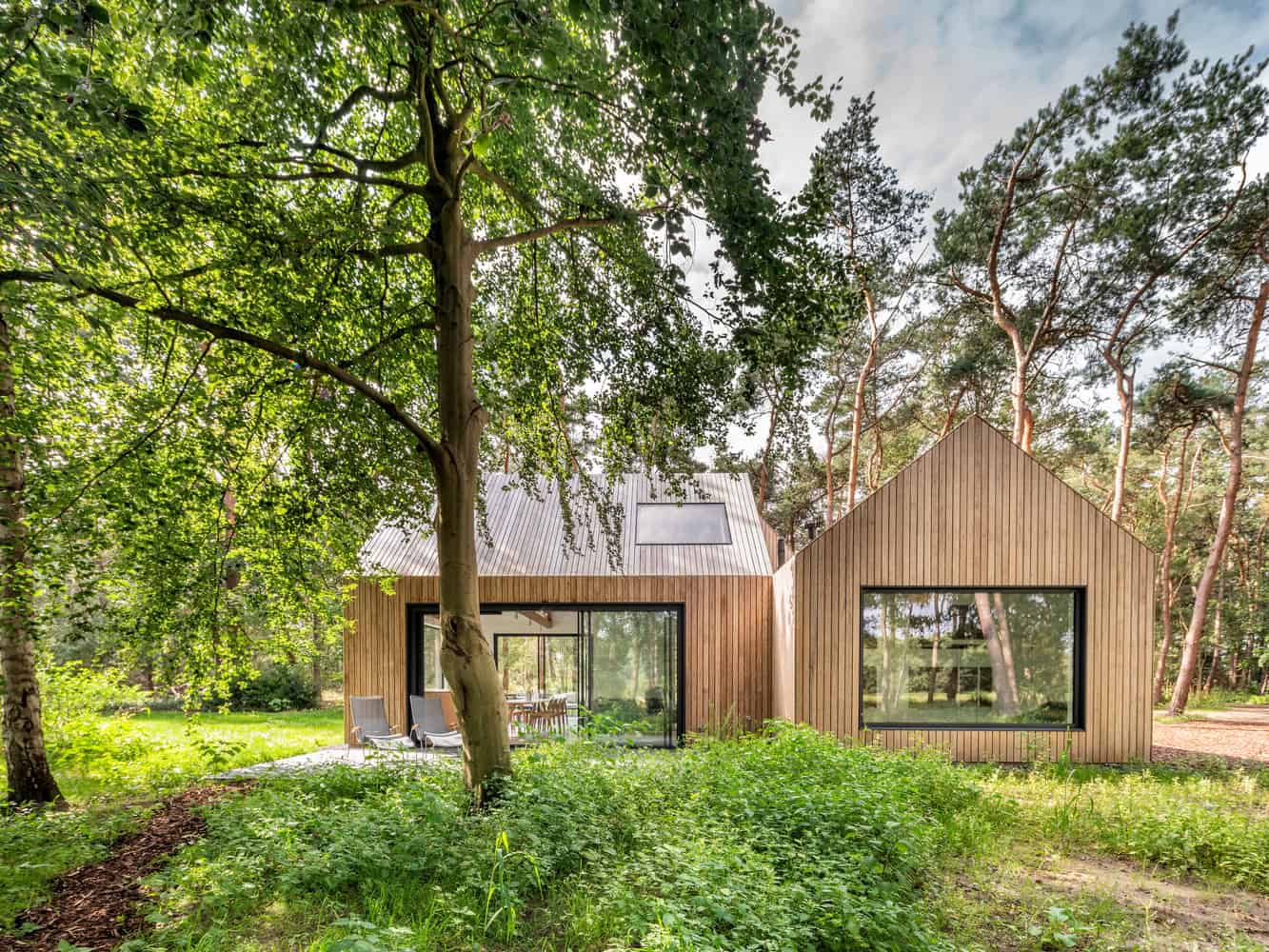 Modern wooden house with minimalist design, large windows, and surrounded by lush greenery in a serene forest setting.