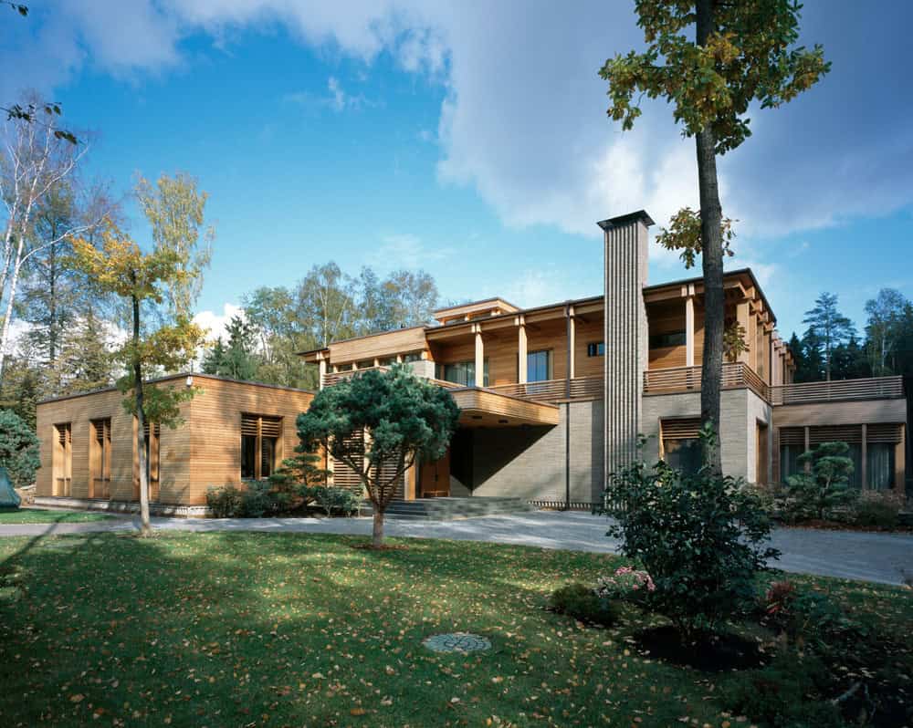 Modern wooden house with contemporary architecture surrounded by lush greenery and tall trees, featuring large windows, a spacious balcony, and natural materials for a stylish, eco-friendly design.
