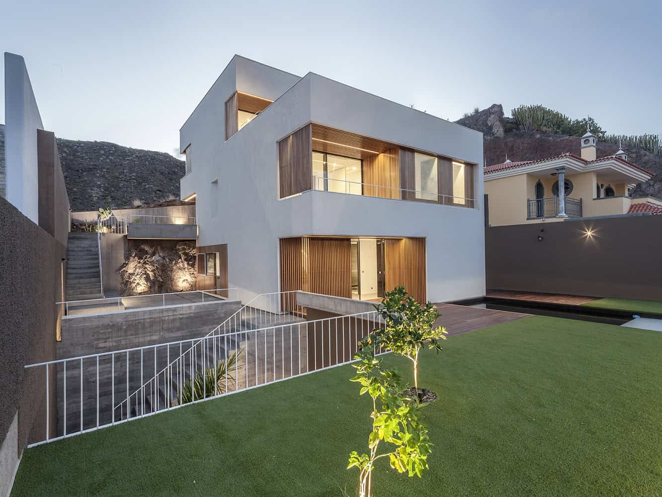 Contemporary modern house exterior with sleek white facade, wooden accents, large glass windows, and landscaped yard showcasing innovative architecture design.