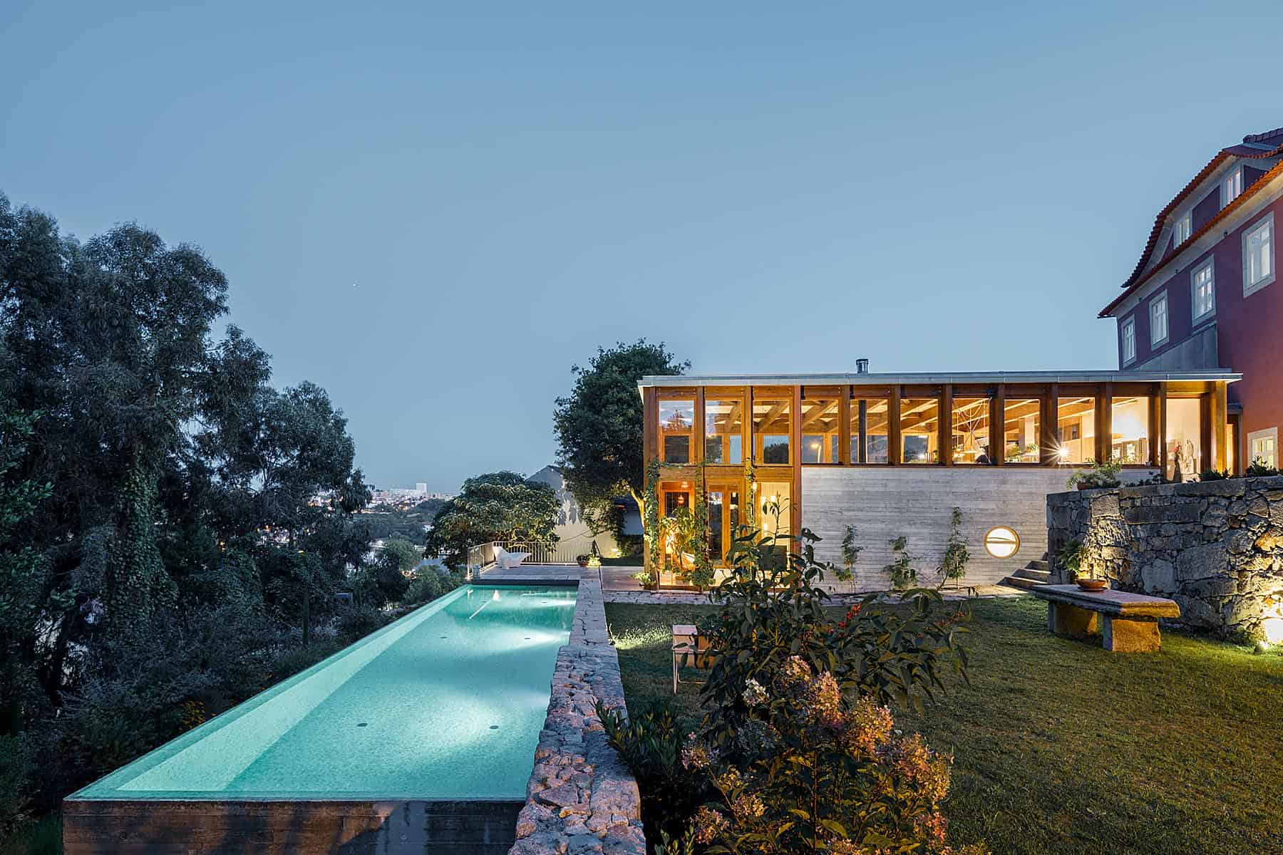 Modern house with infinity pool and wooden accents, surrounded by lush greenery, during twilight, showcasing contemporary architecture and luxurious outdoor living space.