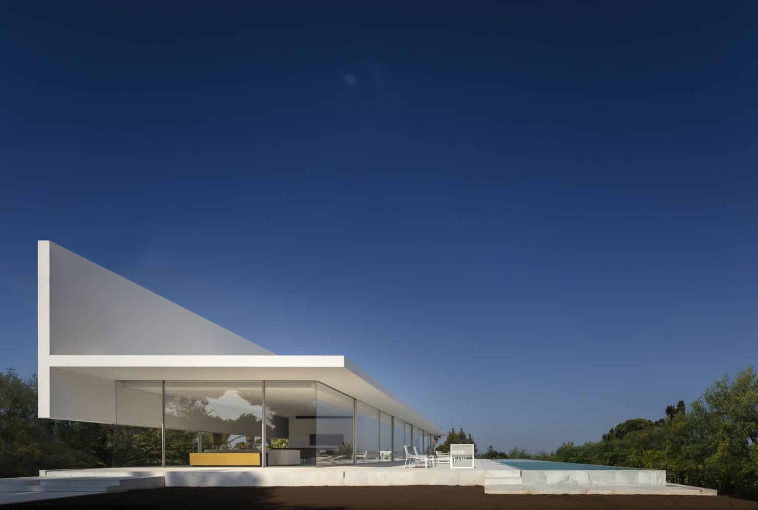Modern minimalist house with sleek white design, large glass windows, and contemporary architecture, set against a clear blue sky for stylish outdoor living.