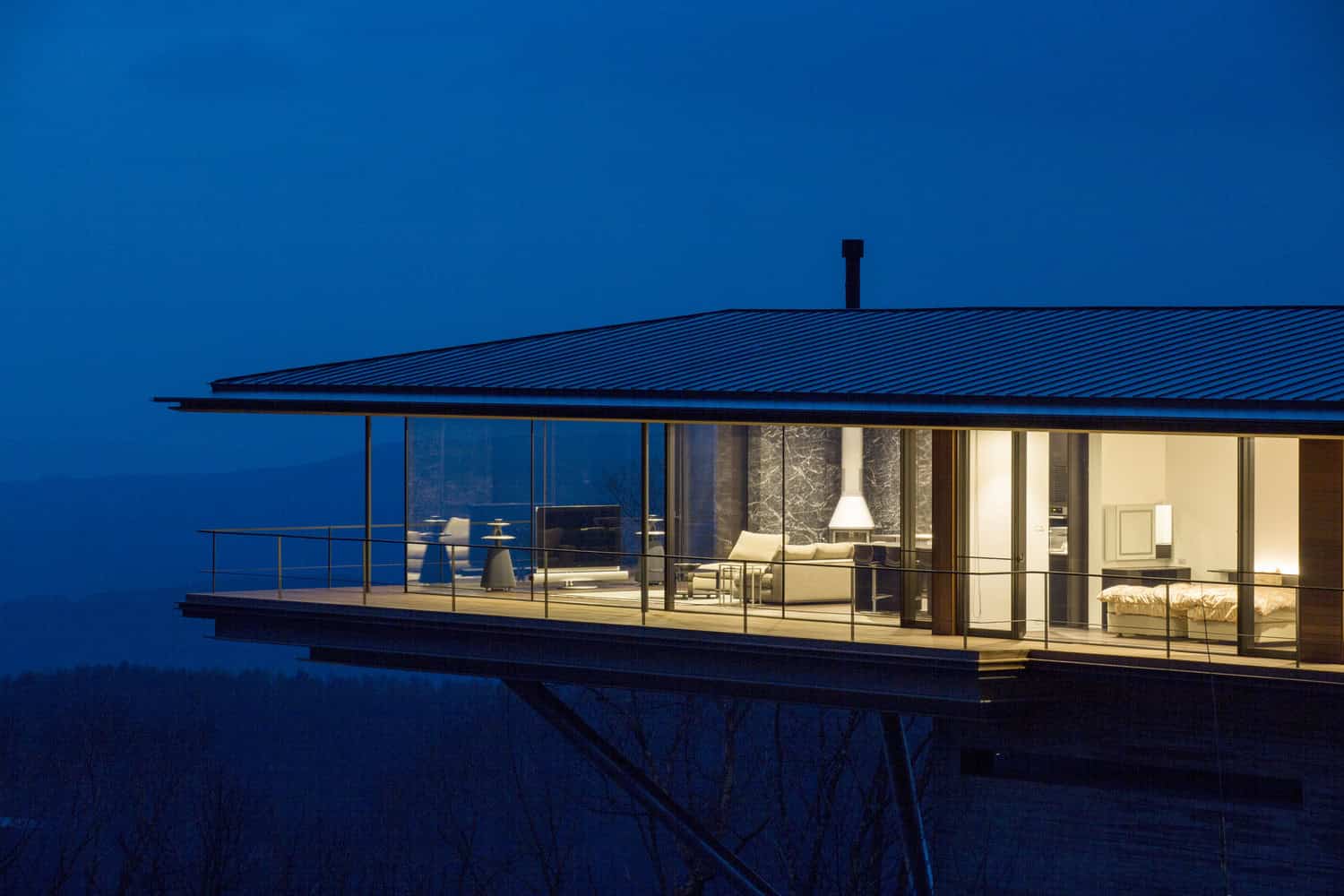 Stunning modern house with glass walls and an outdoor balcony, illuminated at night, showcasing contemporary architecture and innovative design.