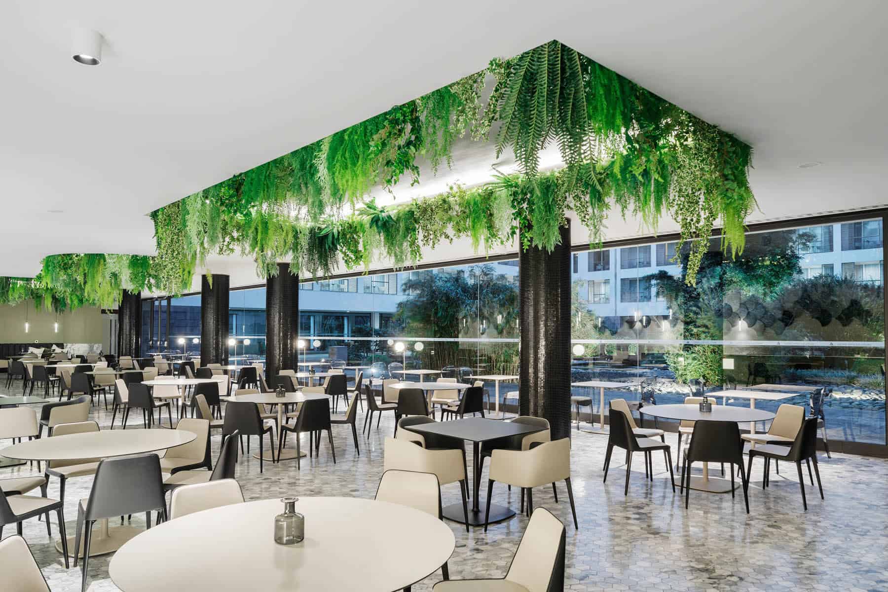 Lush indoor vertical garden with hanging ferns and greenery in modern restaurant interior.