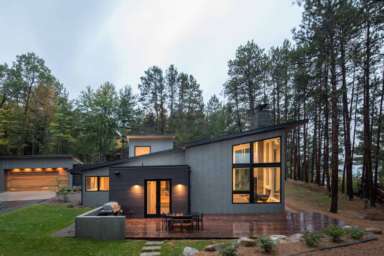 Contemporary modern house with sleek design, large windows, and sloped roof surrounded by tall pine trees, blending minimalist architecture with nature.