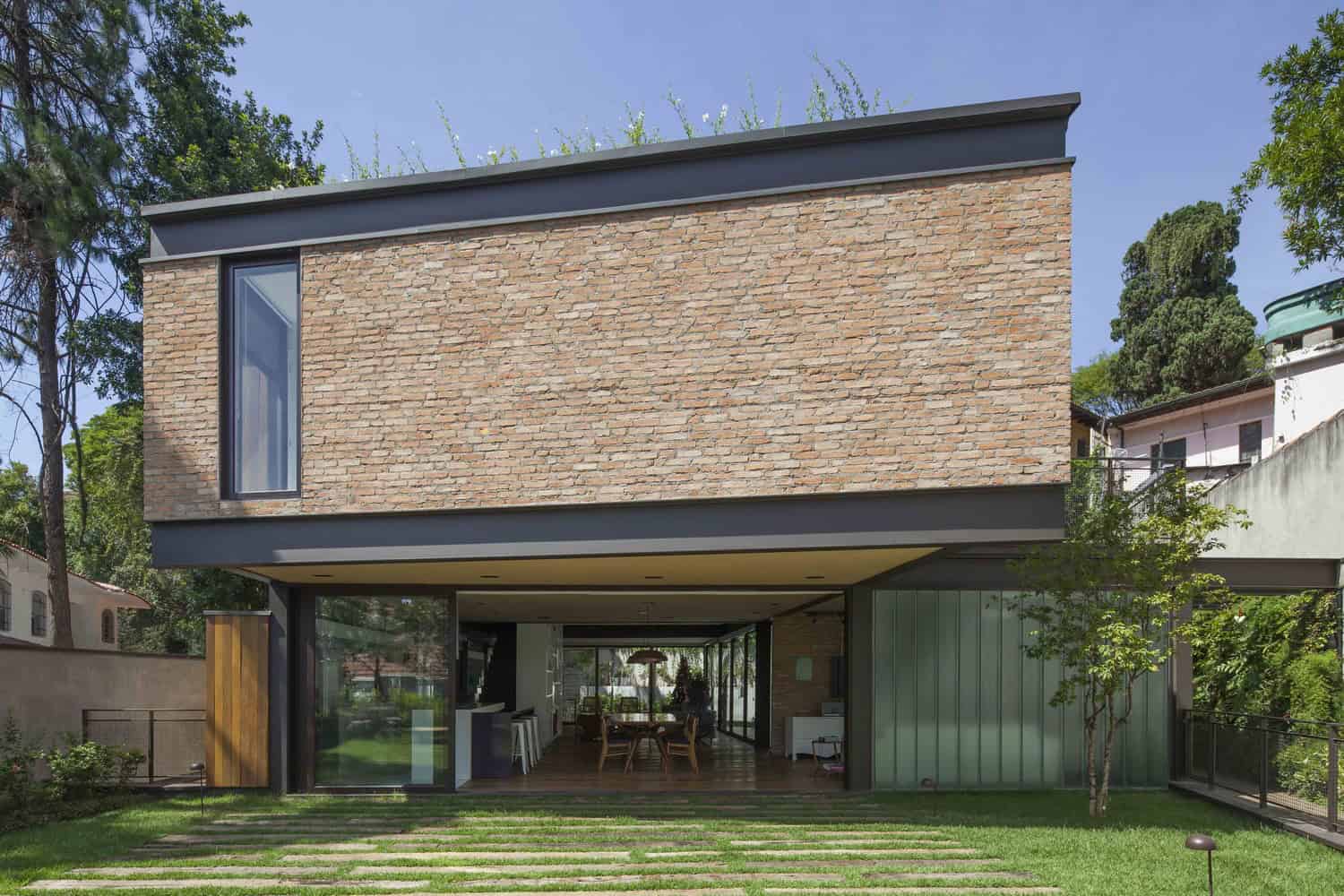 Modern brick and glass house exterior with contemporary architectural design, featuring sleek lines, large windows, and lush front yard landscaping.