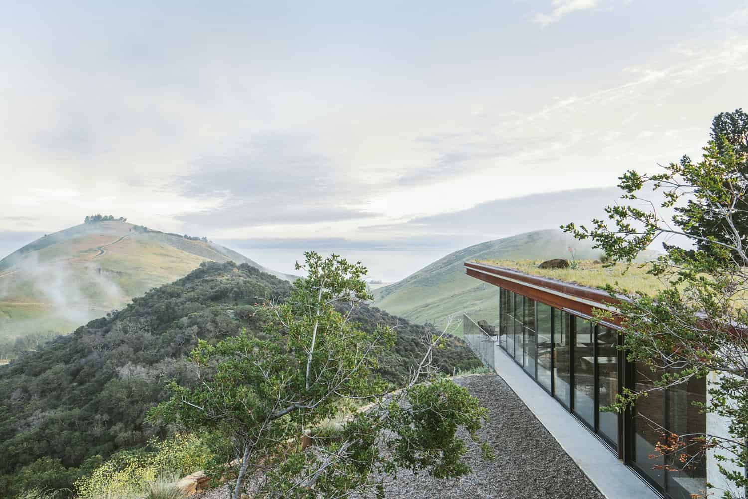 Modern glass house overlooking scenic rolling hills and lush greenery, blending contemporary architecture with natural landscape, perfect for nature lovers and architectural enthusiasts.