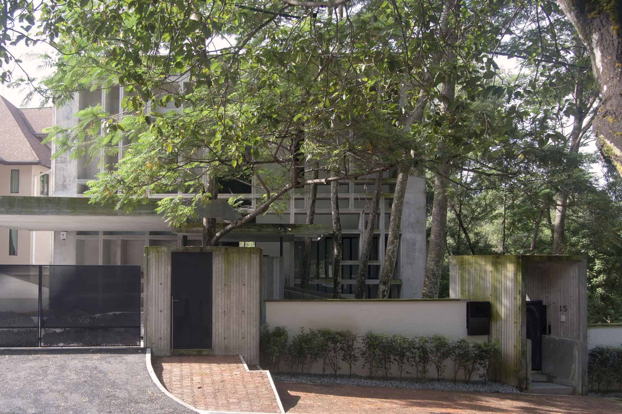 Modern concrete house with innovative architectural design surrounded by lush greenery and mature trees.