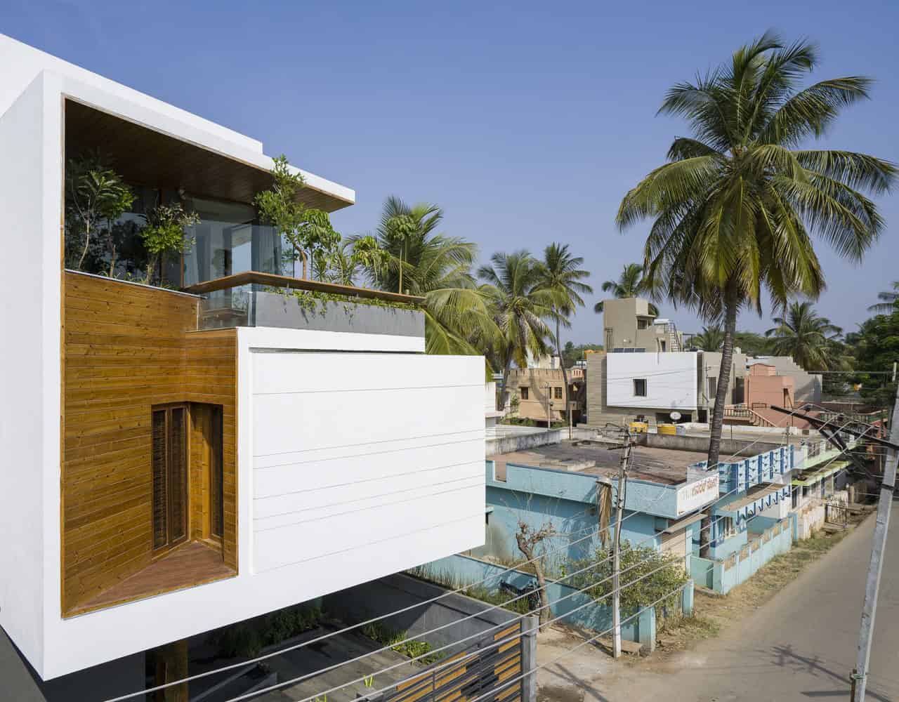 Modern tropical architecture featuring a contemporary white building with wood accents and lush greenery, set against a backdrop of palm trees and vibrant urban surroundings.