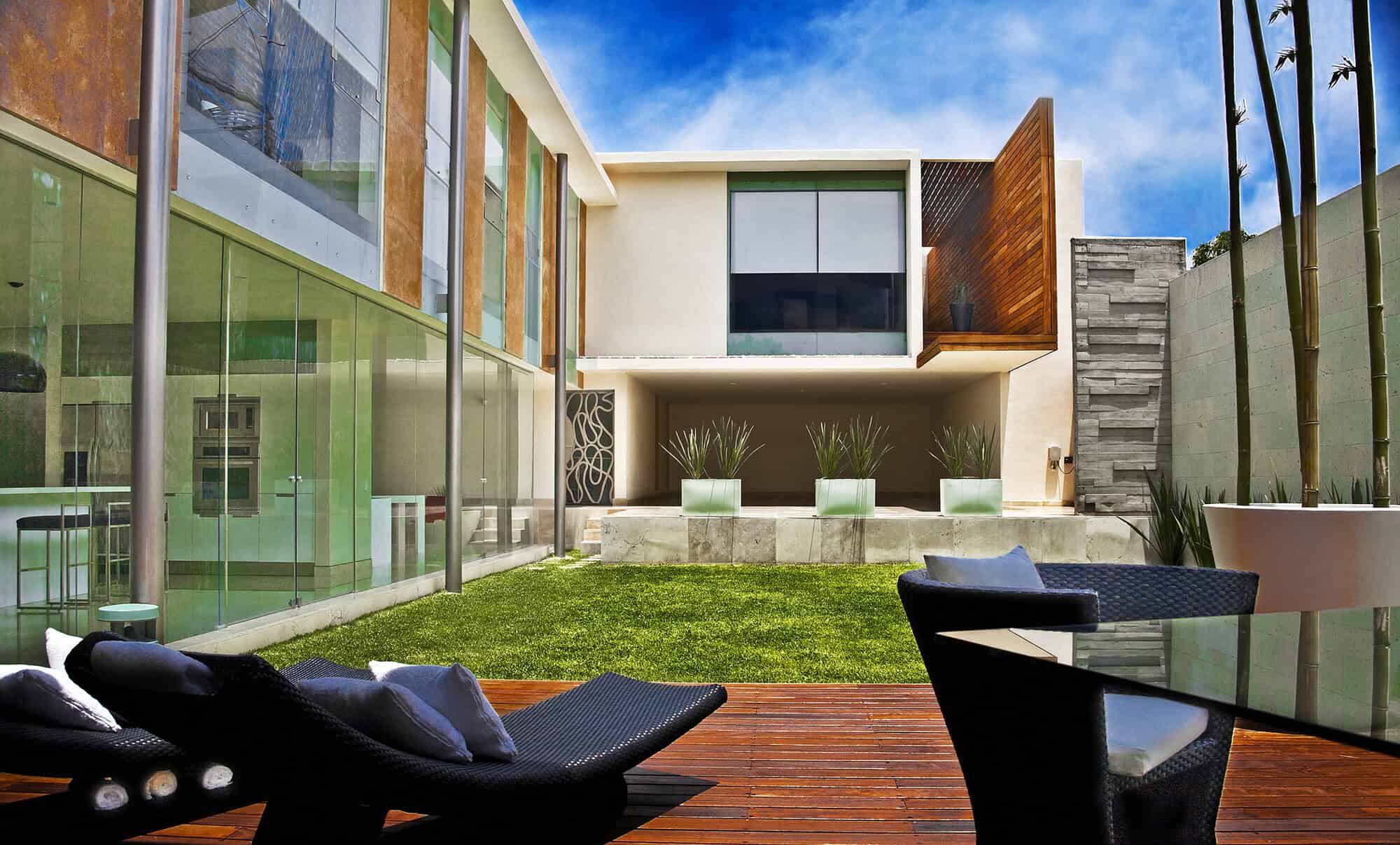 Modern luxury house with glass walls, landscaped garden, contemporary outdoor furniture, and sleek architectural design emphasizing clean lines and natural materials.