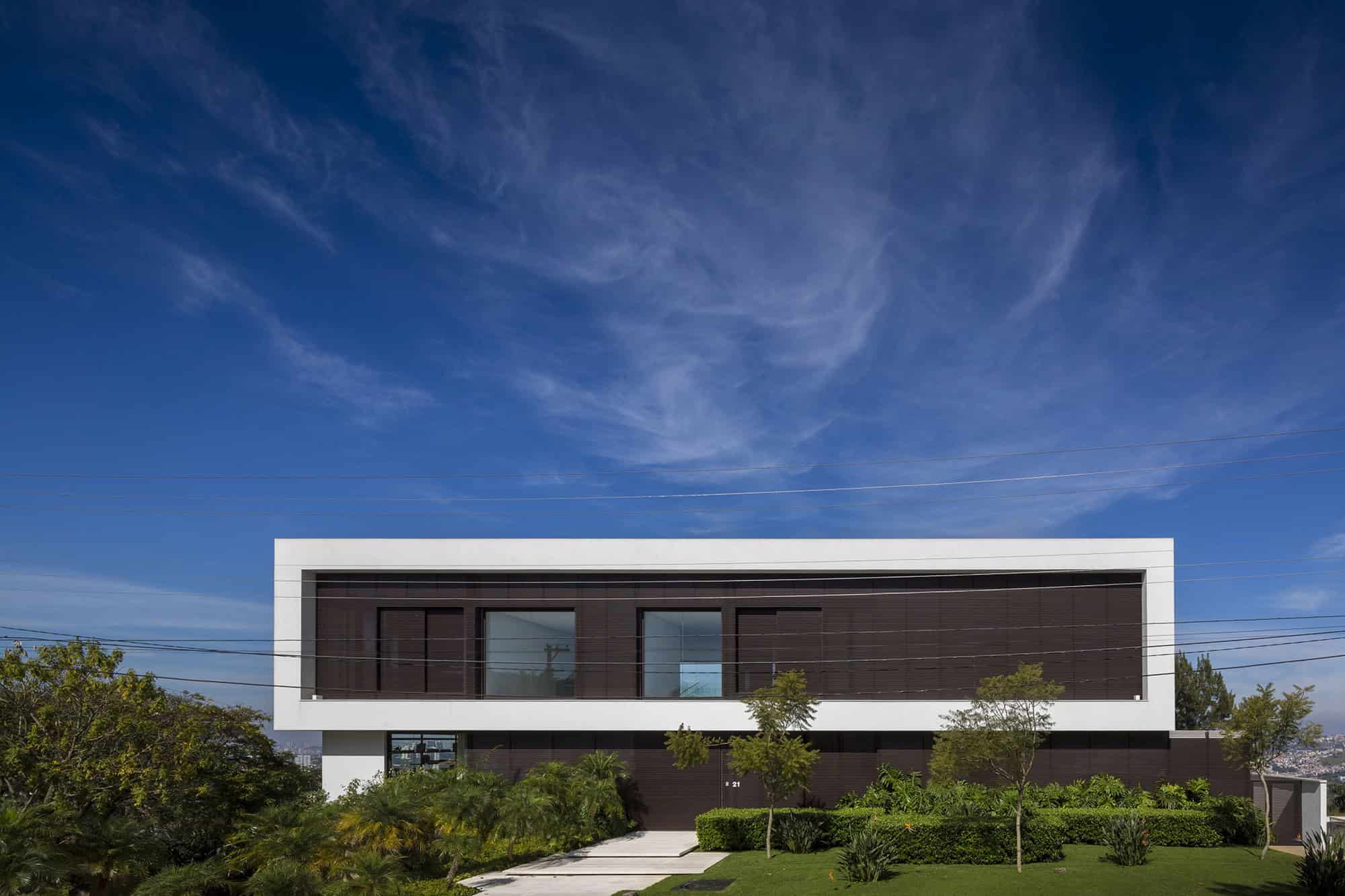 Modern minimalist house with clean lines and large glass windows, set against a blue sky and lush greenery, showcasing contemporary architecture and innovative design.