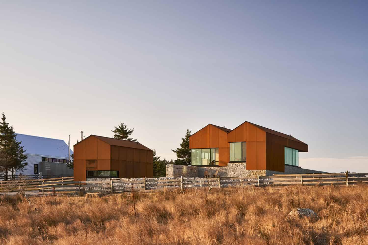 Contemporary modern house with striking rust-colored exterior and large glass windows, set in a scenic landscape with natural grass and trees, showcasing innovative architecture and creative design.